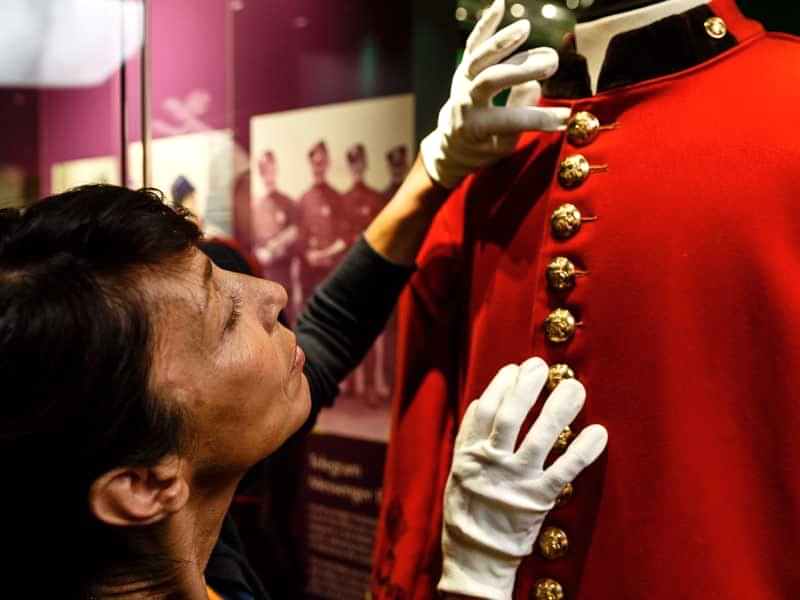 A conservator working on a red coach guard uniform in The Postal Museum exhibition.