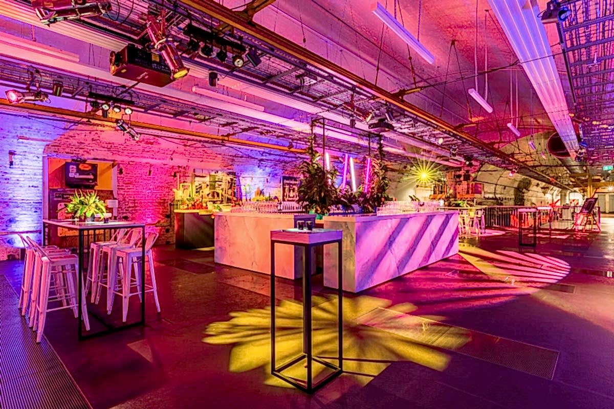 An underground venue room decorated with pink chairs, tables with flowers, and pink and yellow lighting. The Mail Rail tunnels are visible in the background.