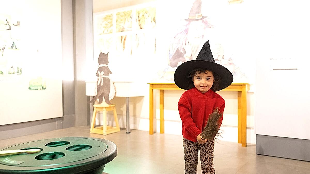 A child wearing a witch hat in the museum exhibition space.