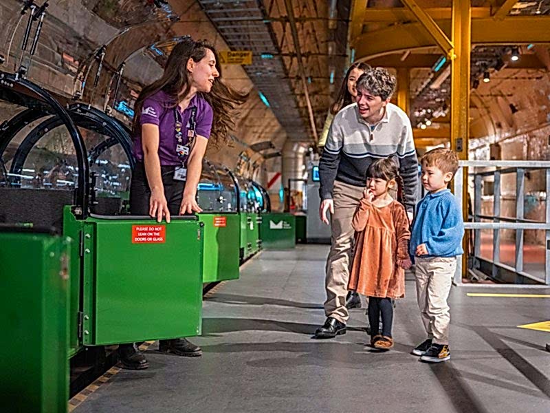A family waiting to board the green miniature Mail Rail train at The Postal Museum.