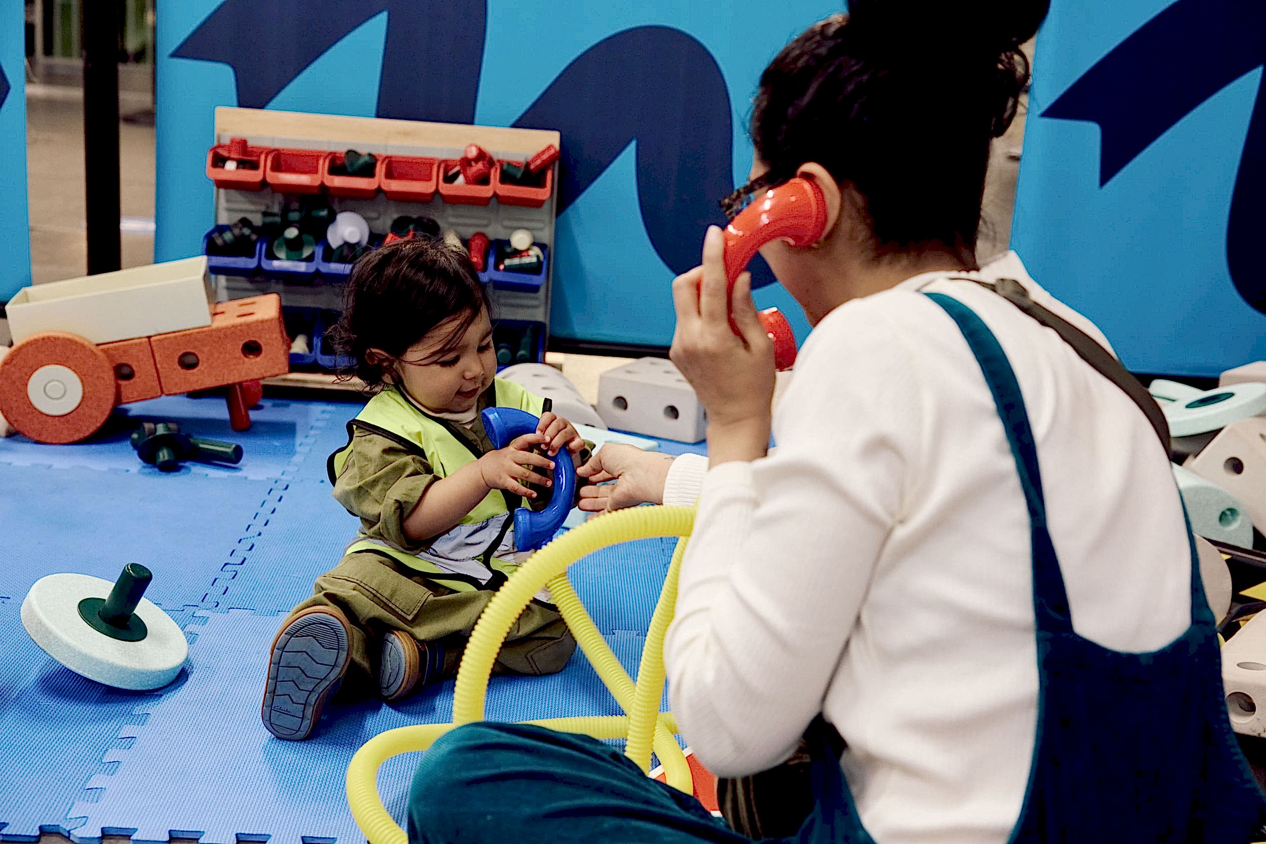 A mum 'answers' a call from her toddler on bright red toy phones with thick yellow tube as the cords.