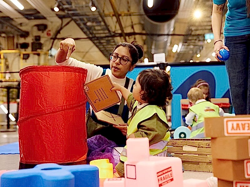 A young boy hands his mum a cardboard envelope to 'post' in a popup red Post Box.