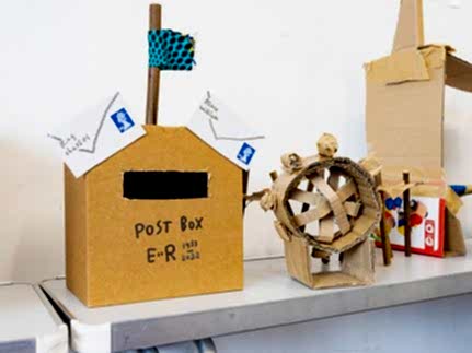 A cardboard postbox and wheel on a craft table.