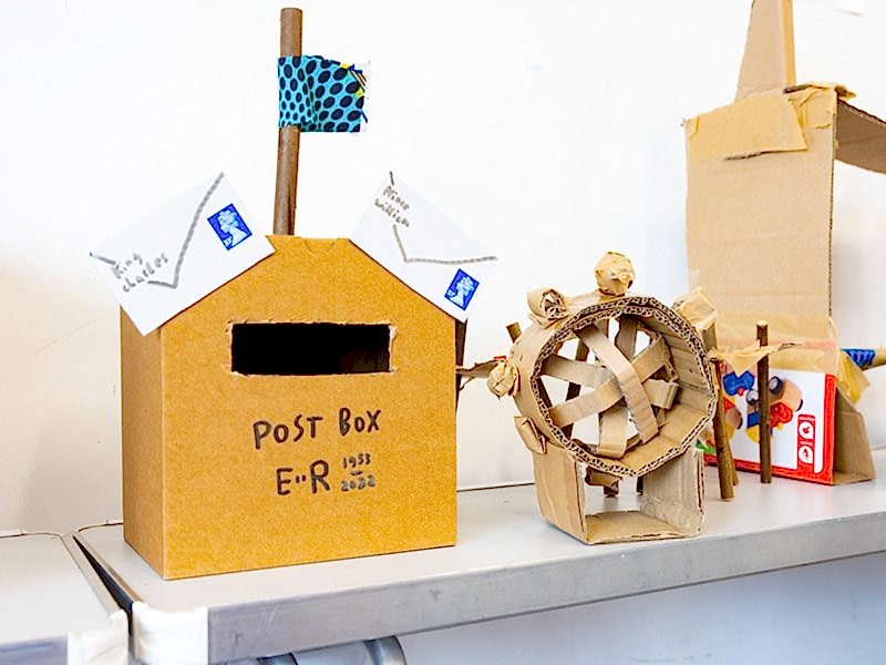 A cardboard postbox and wheel on a craft table.