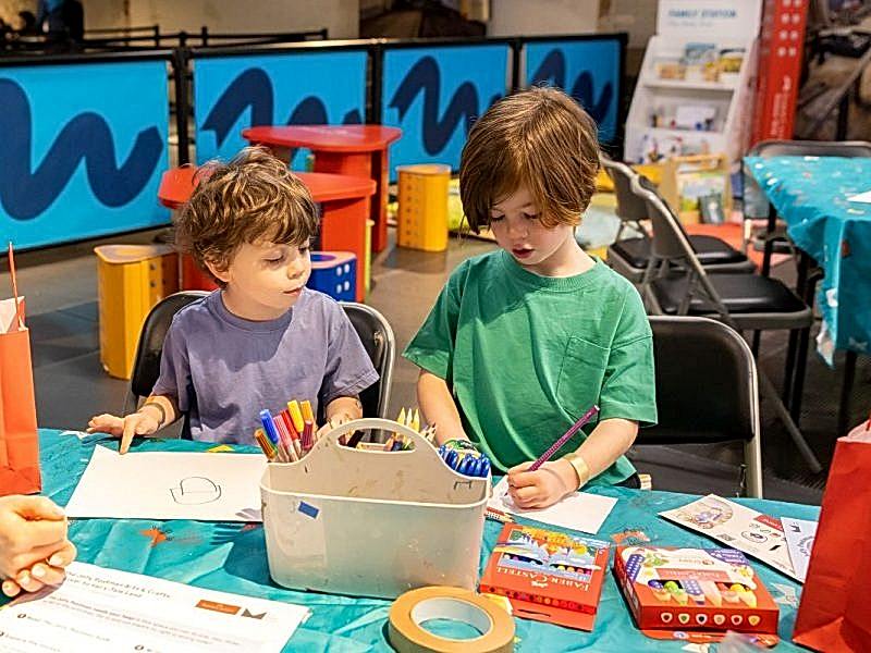Two children playing with colouring pens and paper at a crafts table.